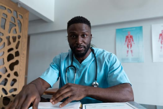 African american male doctor at desk talking and gesturing during video call consultation. telemedicine, online healthcare services during quarantine lockdown.