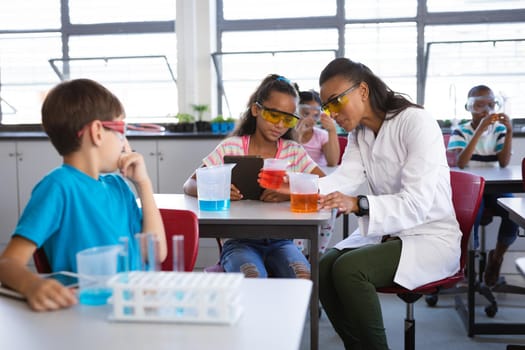 African american female teacher teaching chemistry to a girl during science class at laboratory. school and education concept