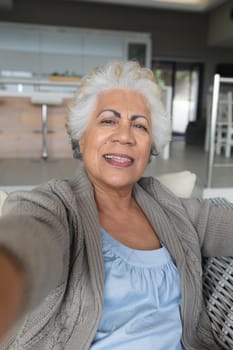 Portrait of mixed race senior woman sitting on sofa making video call. staying at home in isolation during quarantine lockdown.