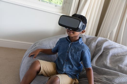 Happy african american boy using vr headset and smiling at home. childhood with technology, spending free time at home.