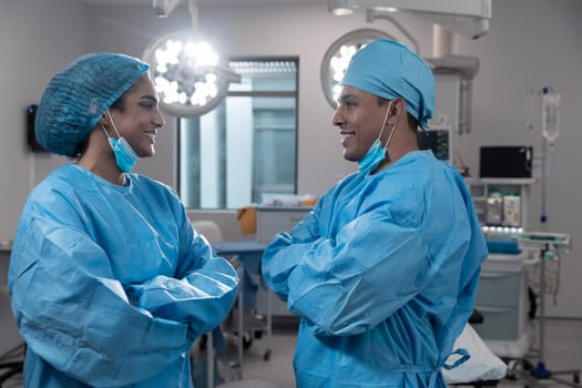 Diverse male and female surgeons wearing face masks and protective clothing in operating theatre. medicine, health and healthcare services during covid 19 coronavirus pandemic.