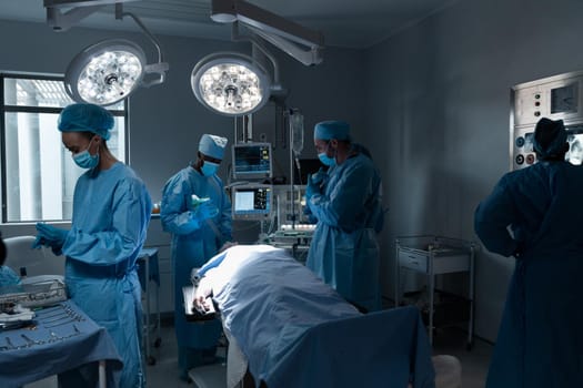 Diverse male and female doctors wearing face masks and surgical overalls in operating theatre. medicine, health and healthcare services during coronavirus covid 19 pandemic.