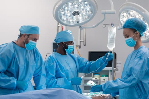 Diverse male and female doctors wearing face masks and surgical overalls in operating theatre. medicine, health and healthcare services during coronavirus covid 19 pandemic.