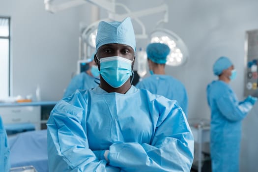 African american male surgeon with face mask and protective clothing in operating theatre. medicine, health and healthcare services during covid 19 coronavirus pandemic.