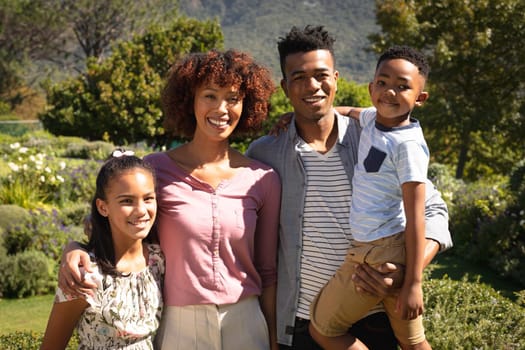 Portrait of happy african american couple with son and daughter outdoors, smiling in sunny garden. family enjoying quality free time together.