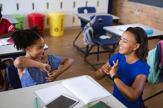African american female teacher and a girl talking in hand sign language at elementary school. school and education concept
