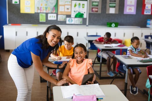 Portrait of african american female teacher and disabled girl smiling in class at elementary school. school and education concept