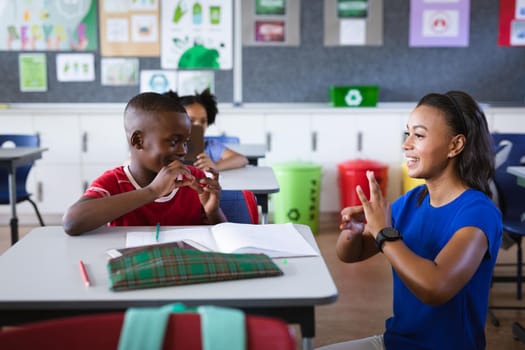 African american female teacher and boy talking in hand sign language at elementary school. school and education concept