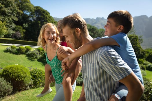 Happy caucasian couple with daughter and son outdoors, playing in sunny garden. family enjoying quality free time together.