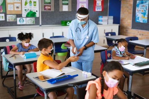 Female health worker spraying hand sanitizer on hands of boy at elementary school. education back to school health safety during covid19 coronavirus pandemic.