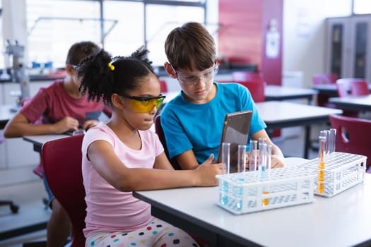 African american girl and caucasian boy using digital tablet in science class at elementary school. school and education concept