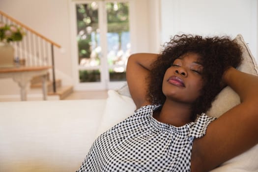 Portrait of african american woman with eyes closed reclining on sofa at home. domestic lifestyle, enjoying leisure time at home.