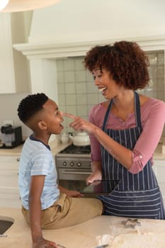Happy african american mother with son baking in kitchen, having fun and using tablet. family enjoying quality free time together.