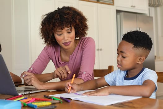 Happy african american mother and son doing homework at home smiling. family domestic life, spending time learning together at home.