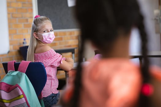 Caucasian girl wearing face mask sitting on her desk in the class at school. education back to school health safety during covid19 coronavirus pandemic