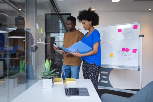 Diverse male and female colleagues standing having discussion with whiteboard in background. independent creative design business.