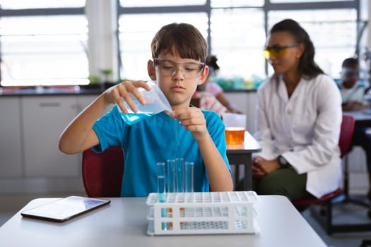 Caucasian boy pouring chemical from beaker into the test tube in science class at laboratory. school and education concept