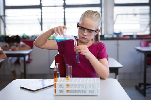 Caucasian girl pouring chemical from beaker into test tube in science class at laboratory. school and education concept