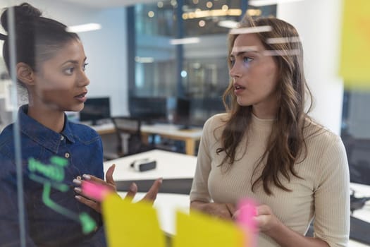 Two diverse female creative colleagues talking at meeting brainstorming. modern office of a creative design business.