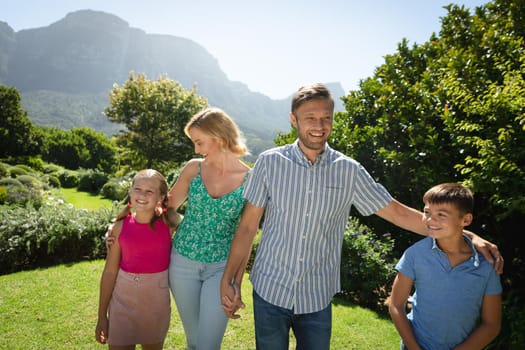 Happy caucasian couple with daughter and son outdoors, walking in sunny garden. family enjoying quality free time together.