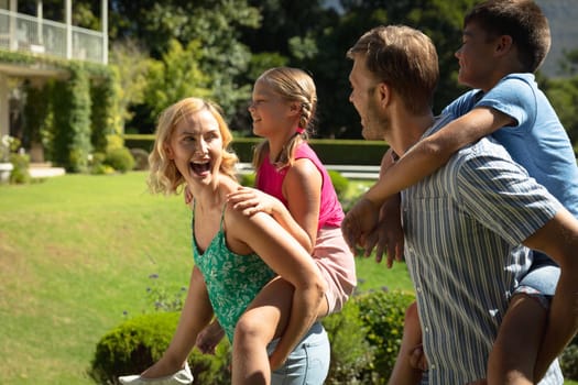 Happy caucasian couple with daughter and son outdoors, playing in sunny garden. family enjoying quality free time together.