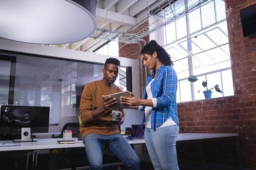 Diverse male and female colleagues at work standing discussing over coffee and tablet. independent creative design business.