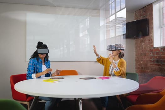 Diverse female colleagues sitting at work wearing virtual reality set and playing. independent creative design business.