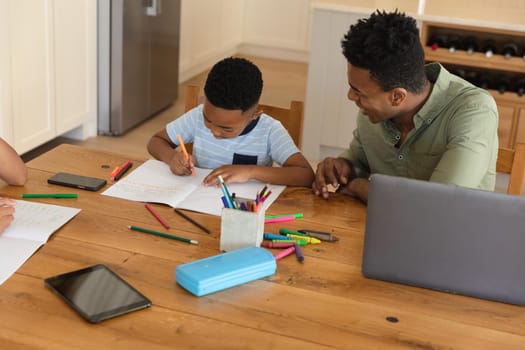 Happy african american father with daughter and son doing homework at home smiling. family domestic life, spending time working together at home.