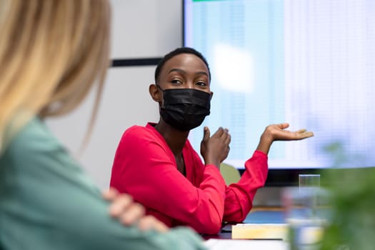 African american businesswoman wearing mask pointing at monitor. working in a modern office during covid 19 coronavirus pandemic.