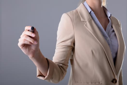 Midsection of caucasian businesswoman holding pen, isolated on grey background. business, technology, communication and growth concept.