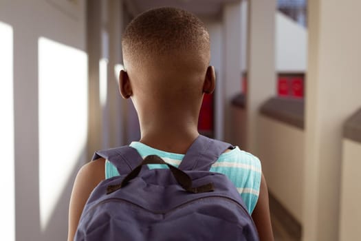 Rear view of african american schoolboy wearing schoolbag standing in school corridor. childhood and education at elementary school.