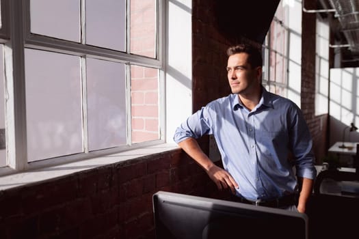 Thoughtful caucasian businessman standing in sunny office looking out of window. working in business at a modern office.