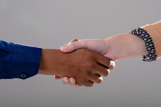 Midsection of caucasian and african american business people shaking hands on grey background. business, technology, communication and growth concept.