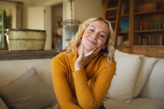 Portrait of happy caucasian woman sitting on couch in luxury living room, leaning on hand, smiling. spending free time at home.