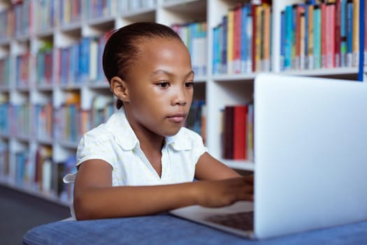 African american schoolgirl at desk in school library concentrating using laptop. childhood, technology and education at elementary school.