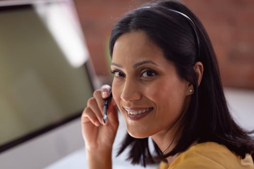 Portrait of happy caucasian businesswoman wearing phone headset sitting at desk turning and smiling. working in business at a modern office.