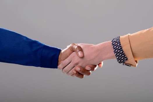 Midsection of caucasian and african american business people shaking hands on grey background. business, technology, communication and growth concept.