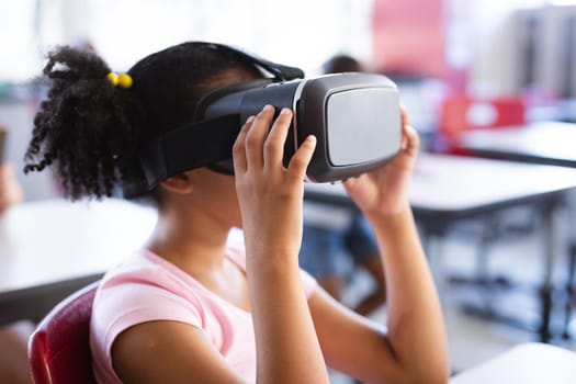 African american girl wearing vr headset while sitting on her desk in the class at school. school and education concept