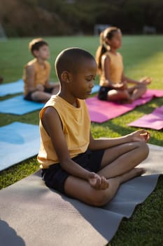 African american boy practicing yoga and meditating sitting on yoga mat in the garden at school. school and education concept