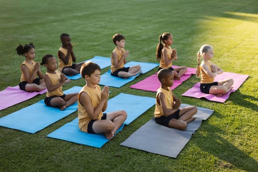 Group of diverse students practicing yoga and meditating sitting on yoga mat in the garden at school. school and education concept