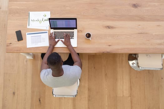 High angle view of african american man sitting at table using laptop working from home. staying at home in isolation during quarantine lockdown.