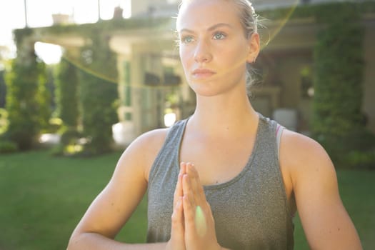 Tranquil caucasian woman practicing yoga in sunny garden, standing with hands pressed together. health, fitness and wellbeing, spending quality time at home.