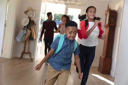 Happy african american couple with son and daughter back from school embracing and smiling at home. family enjoying quality free time together.