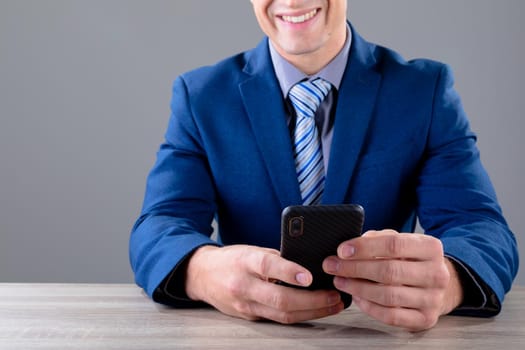 Smiling caucasian businessman using smartphone, isolated on grey background. business technology, communication and growth concept digitally generated composite image.