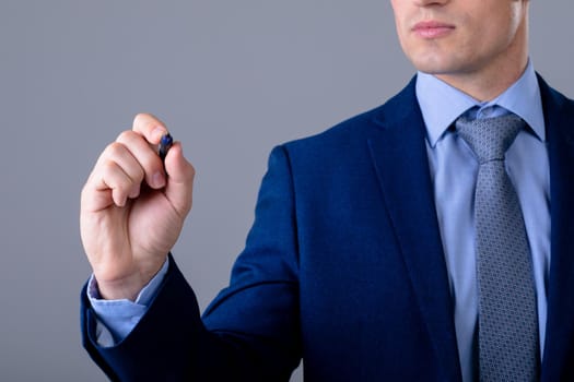 Midsection of caucasian businessman holding pen, isolated on grey background. business technology, communication and growth concept.