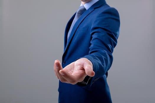 Midsection of caucasian businessman reaching his hand, isolated on grey background. business technology, communication and growth concept.