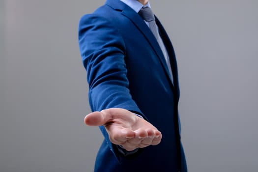 Midsection of caucasian businessman reaching his hand, isolated on grey background. business technology, communication and growth concept.