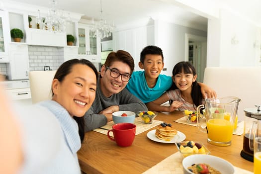 Asian couple with son and daughter sitting at table eating together at home. domestic lifestyle and leisure family time concept.