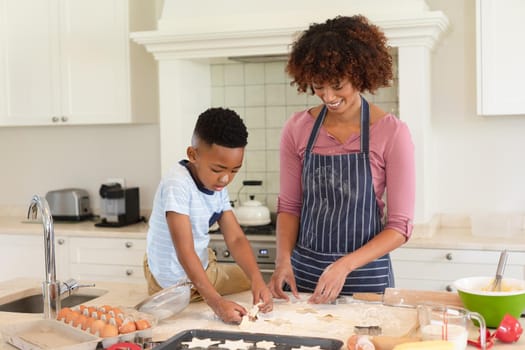 Happy african american mother with son baking in kitchen, cutting cookies. family enjoying quality free time together.