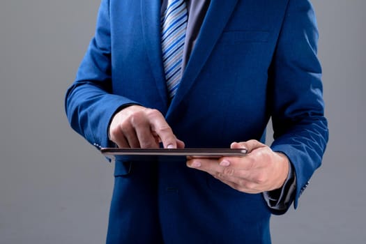 Midsection of caucasian businessman using tablet, isolated on grey background. business technology, communication and growth concept.